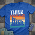 Blue t-shirt with chess design and 'THINK' text on a stone surface